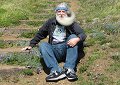 High winds make Bill's beard swirl, making about a 190 degree curl. - Bill is sitting on the trail up the south Twin Peak - near a lupine flower that blooms every spring on these hills.