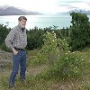 Larry is checking out a wild rose bush - with Lake Tekapo behind him